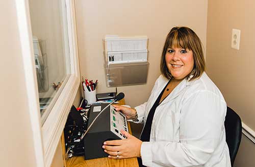 Audiologist Lauren Gromel sitting at her hearing booth equipment.